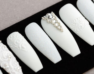 Set of ten white press-on nails with different designs. Some nails have a white glitter finish, some have a white swirl design, and some have a rhinestone design.