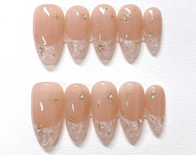 Set of ten nude-colored false nails with a white lace design and gold glitter stars.