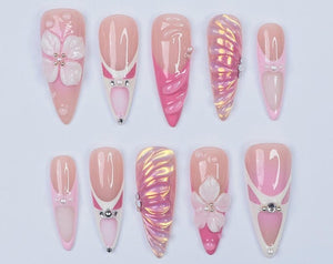 Ten pink and white artificial nails with different designs. Some nails have a flower design, some have a swirl design, and some have a pearl design.