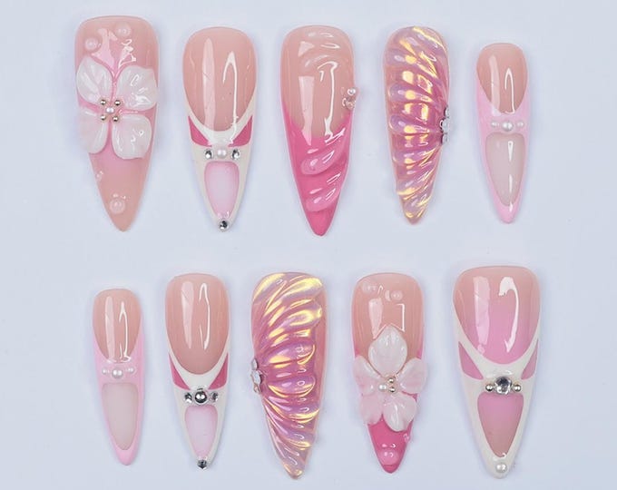 Ten pink and white artificial nails with different designs. Some nails have a flower design, some have a swirl design, and some have a pearl design.