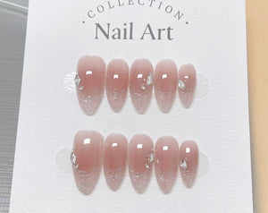 A set of artificial nails with a gradient design, transitioning from a nude pink to a glittery silver at the tips. Each nail is adorned with a small, sparkling gem. The packaging reads "Collection Nai