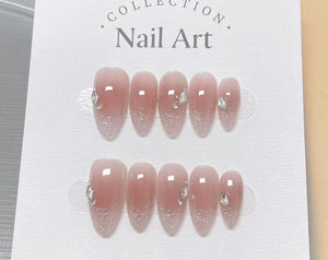 A set of artificial nails with a gradient design, transitioning from a nude pink to a glittery silver at the tips. Each nail is adorned with a small, sparkling gem. The packaging reads "Collection Nai