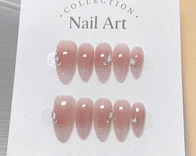 A set of artificial nails with a gradient design, transitioning from a nude pink to a glittery silver at the tips. Each nail is adorned with a small, sparkling gem. The packaging reads "Collection Nai