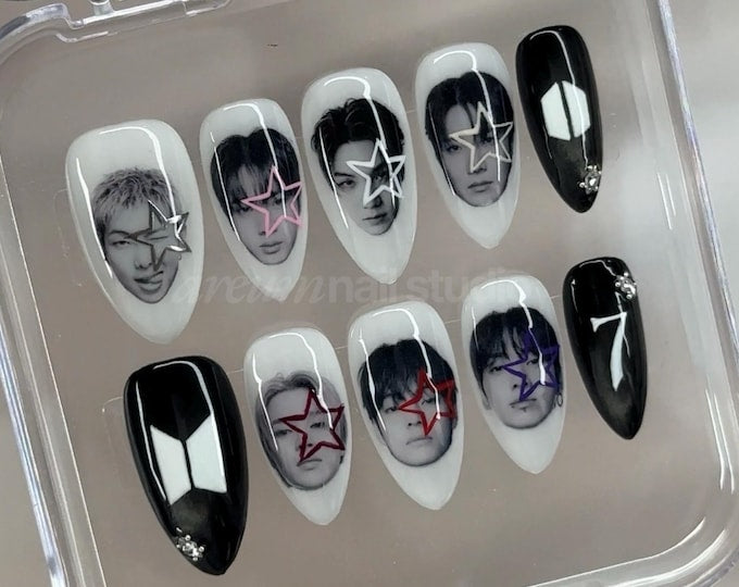 A set of ten almond-shaped press-on nails in a clear plastic case. The nails feature black and white portraits of individuals with colorful star overlays, solid black nails with small rhinestones, and