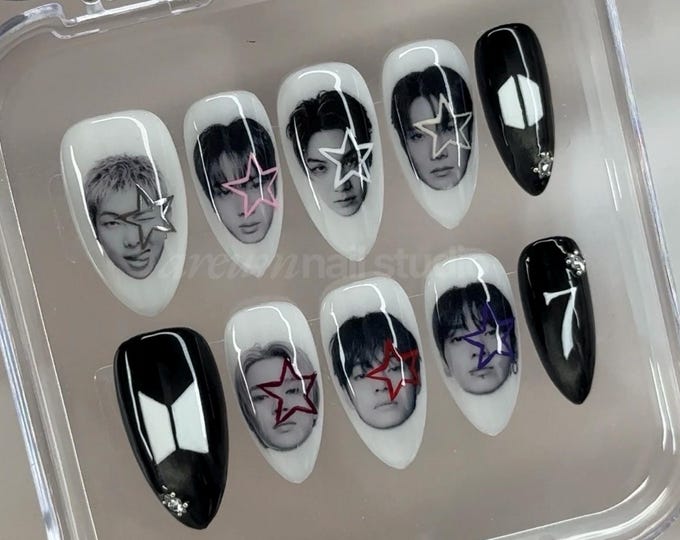 A set of ten almond-shaped press-on nails in a clear plastic case. The nails feature black and white portraits of individuals with colorful star overlays, solid black nails with small rhinestones, and