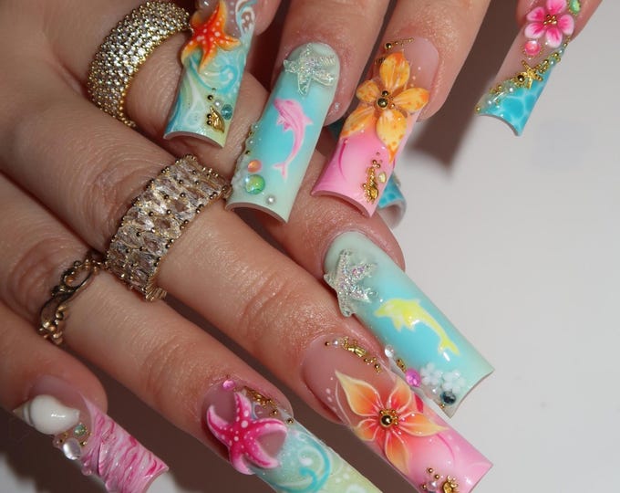 Long square-shaped artificial nails featuring a tropical theme with gradient blue and pink backgrounds. The nail art includes three-dimensional starfish, dolphins, and floral designs, accented with sm