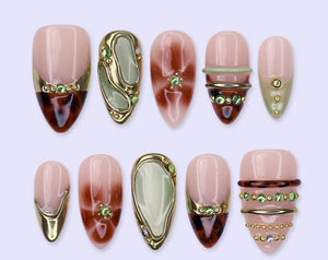 A set of ten almond-shaped press-on nails featuring a mix of designs including tortoiseshell patterns, sage green accents, metallic gold bands, and small green rhinestones. The nails have a glossy fin