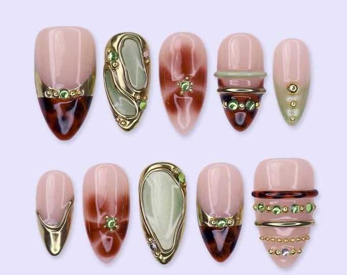 A set of ten almond-shaped press-on nails featuring a mix of designs including tortoiseshell patterns, sage green accents, metallic gold bands, and small green rhinestones. The nails have a glossy fin