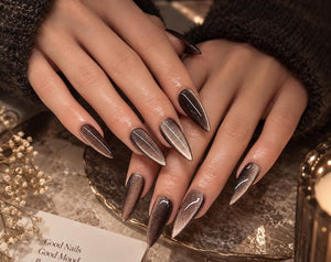 Long, pointed stiletto-shaped nails featuring a dark brown and metallic silver cat-eye magnetic polish effect. A small white card is visible with the printed text: Good Nails, Good Mood, Better Me, fo